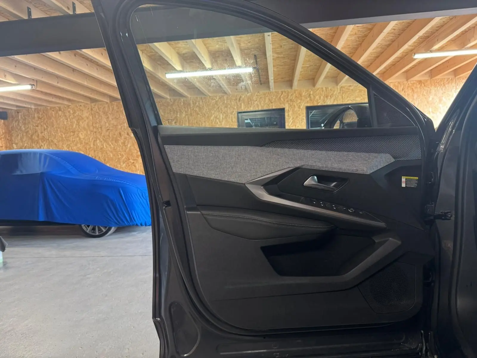 Vue intérieure de la porte avant gauche grise du Peugeot 5008 1.2 Hybrid 136 GT avec habillage tissu et plastique noir.