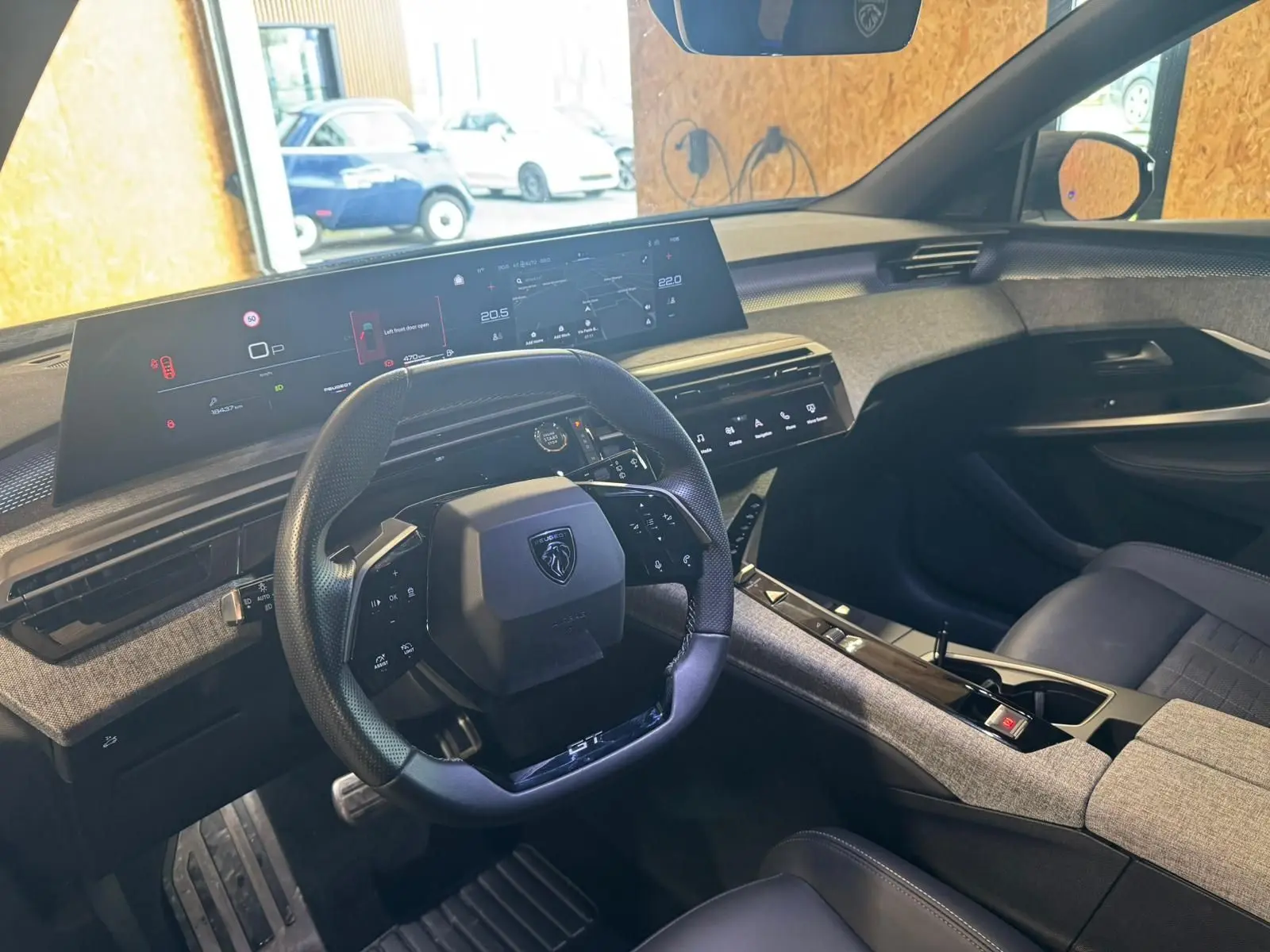 Vue intérieure du poste de conduite du Peugeot 5008 gris 1.2 Hybrid 136 GT, avec volant compact et grand écran numérique panoramique.