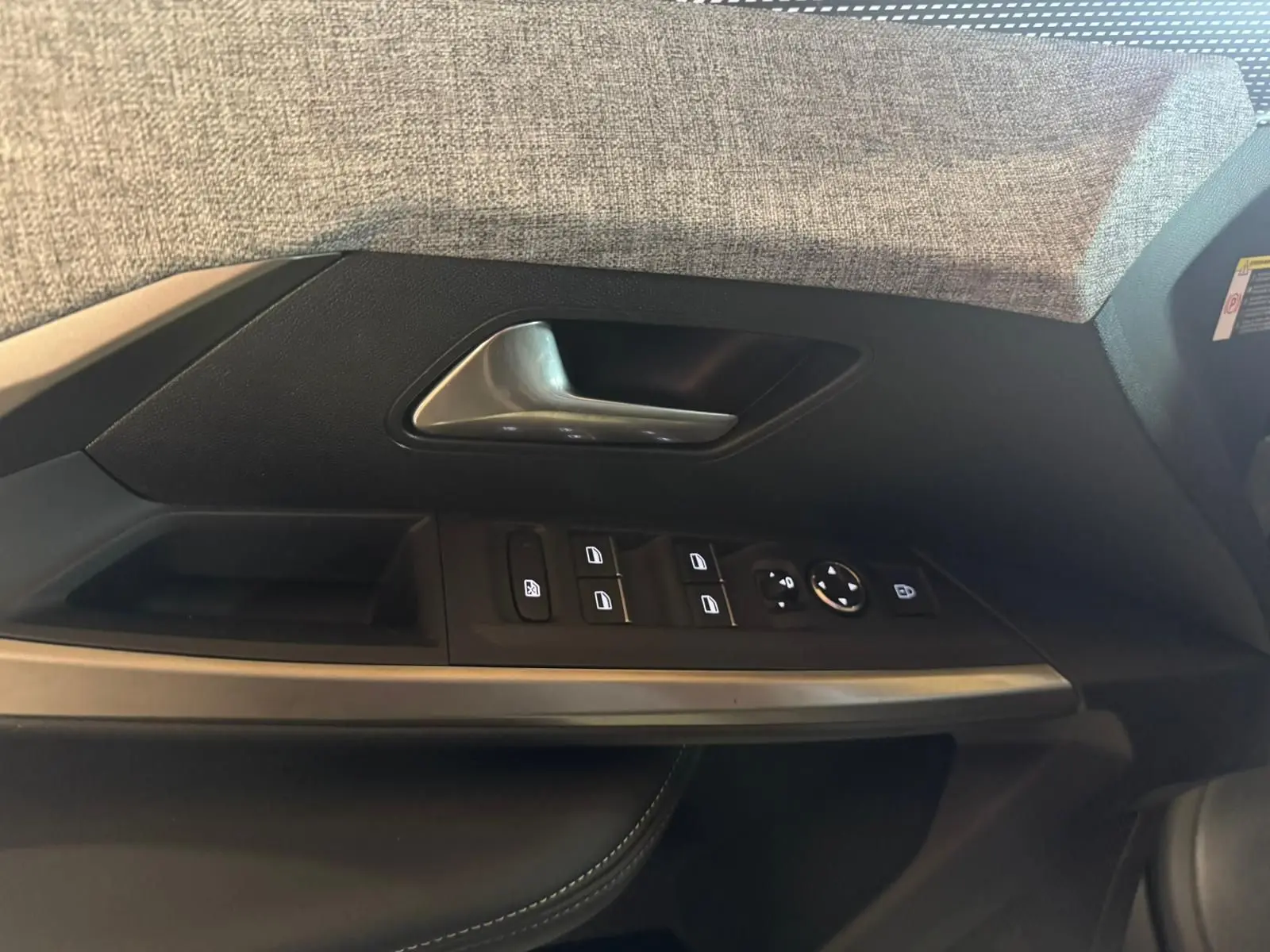 Gros plan sur la garniture de porte côté gauche du Peugeot 5008 gris, avec commandes électriques et poignée argentée.