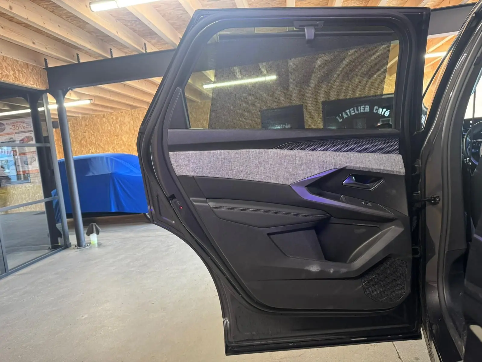 Vue intérieure de la porte arrière droite ouverte d’un Peugeot 5008 gris, avec habillage tissu et plastique noir.