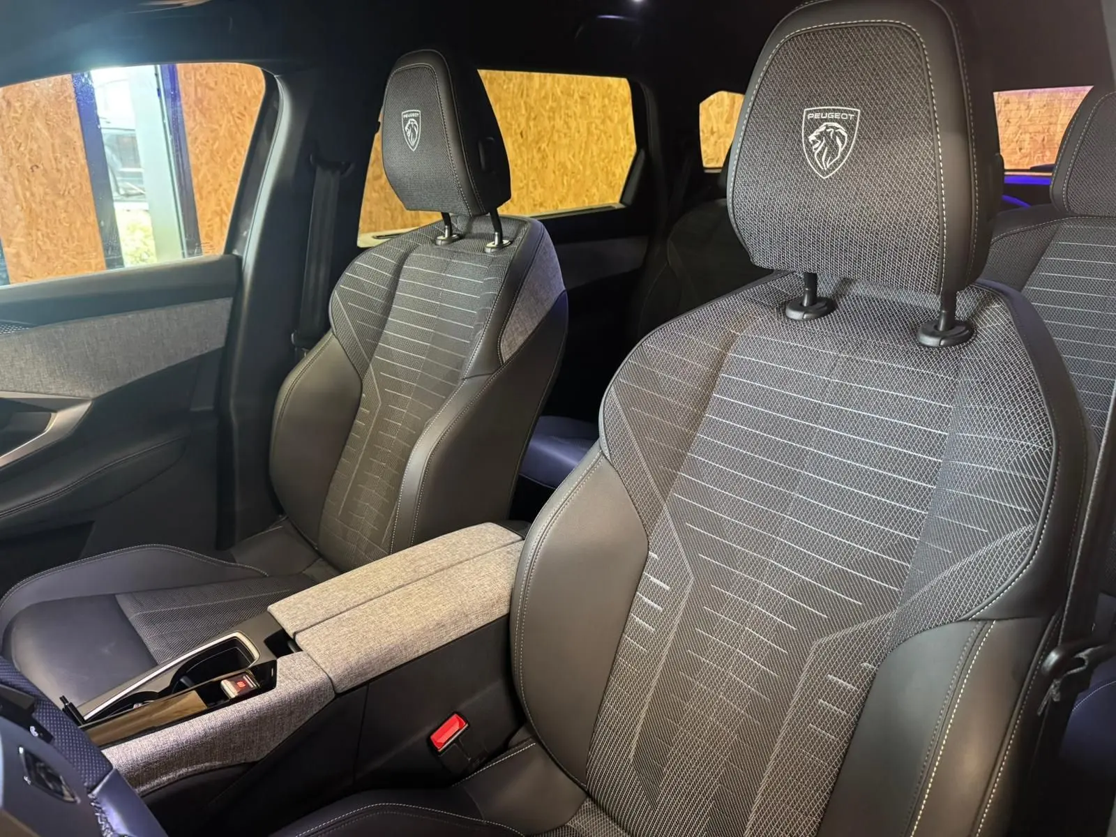 Vue intérieure rapprochée des sièges avant gris tissu et cuir du Peugeot 5008 1.2 HYBRID 136 GT avec logo brodé sur les appuie-têtes.