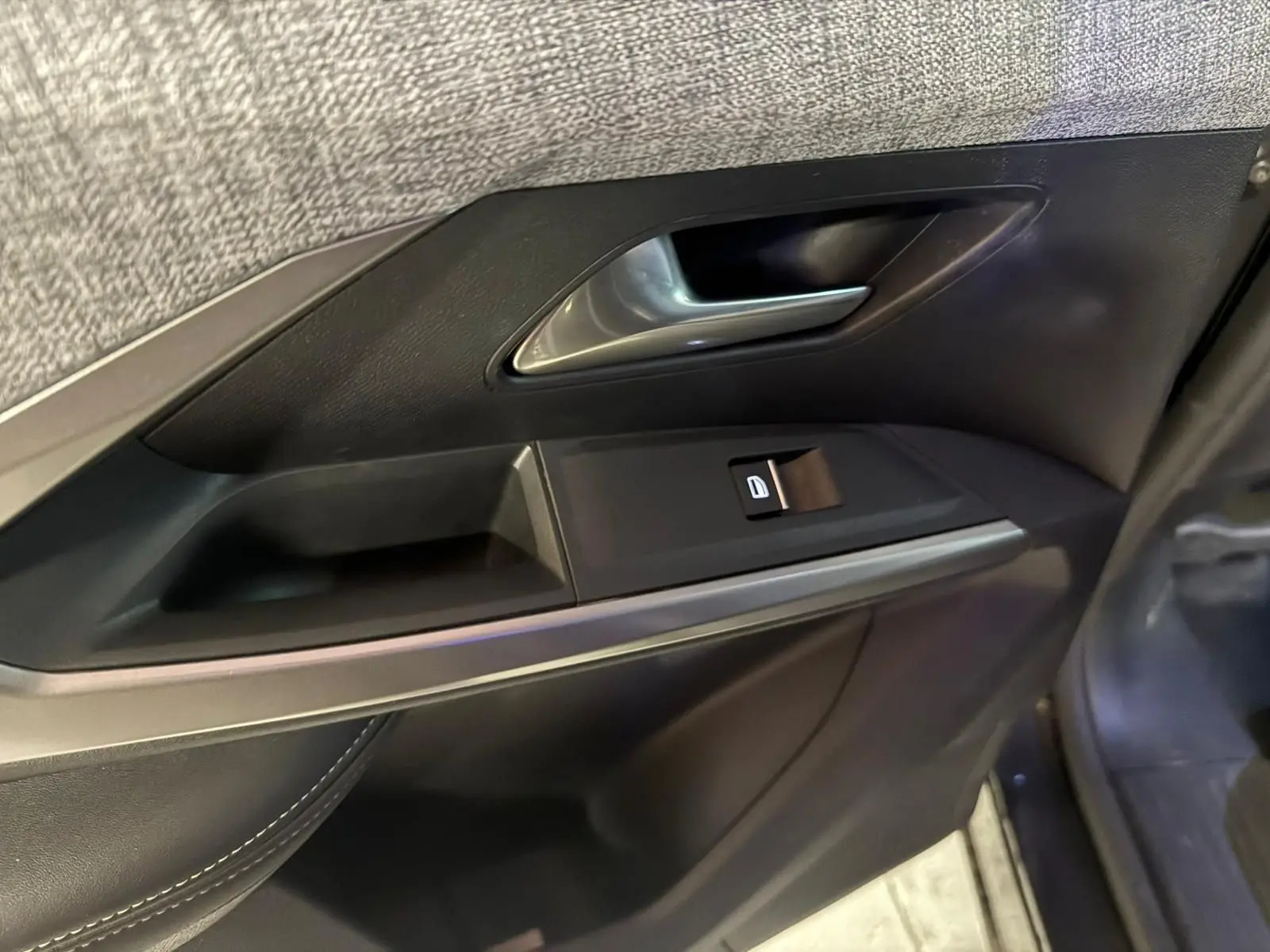 Gros plan sur la poignée intérieure et le bouton de verrouillage de la porte côté gauche d’un Peugeot 5008 gris.