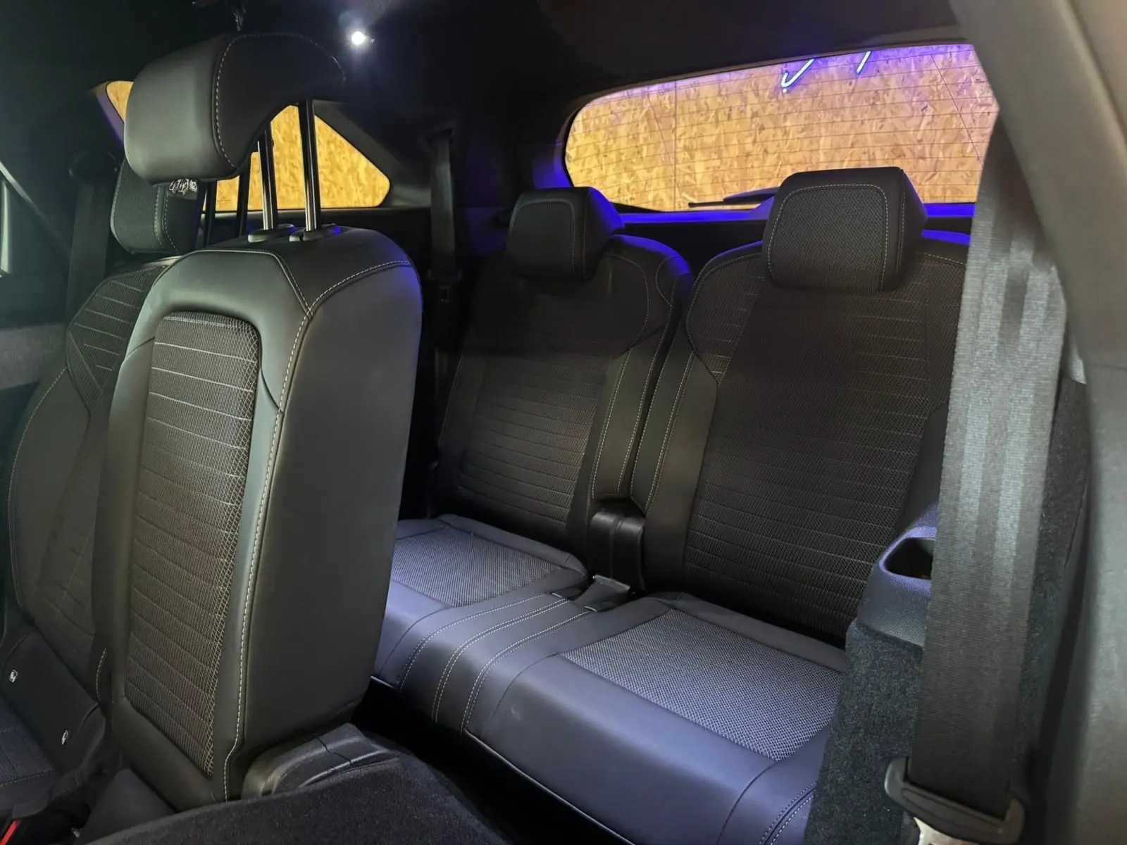 Vue intérieure arrière du Peugeot 5008 1.2 HYBRID 136 GT, sièges tissu noir avec surpiqûres blanches, ambiance tamisée.