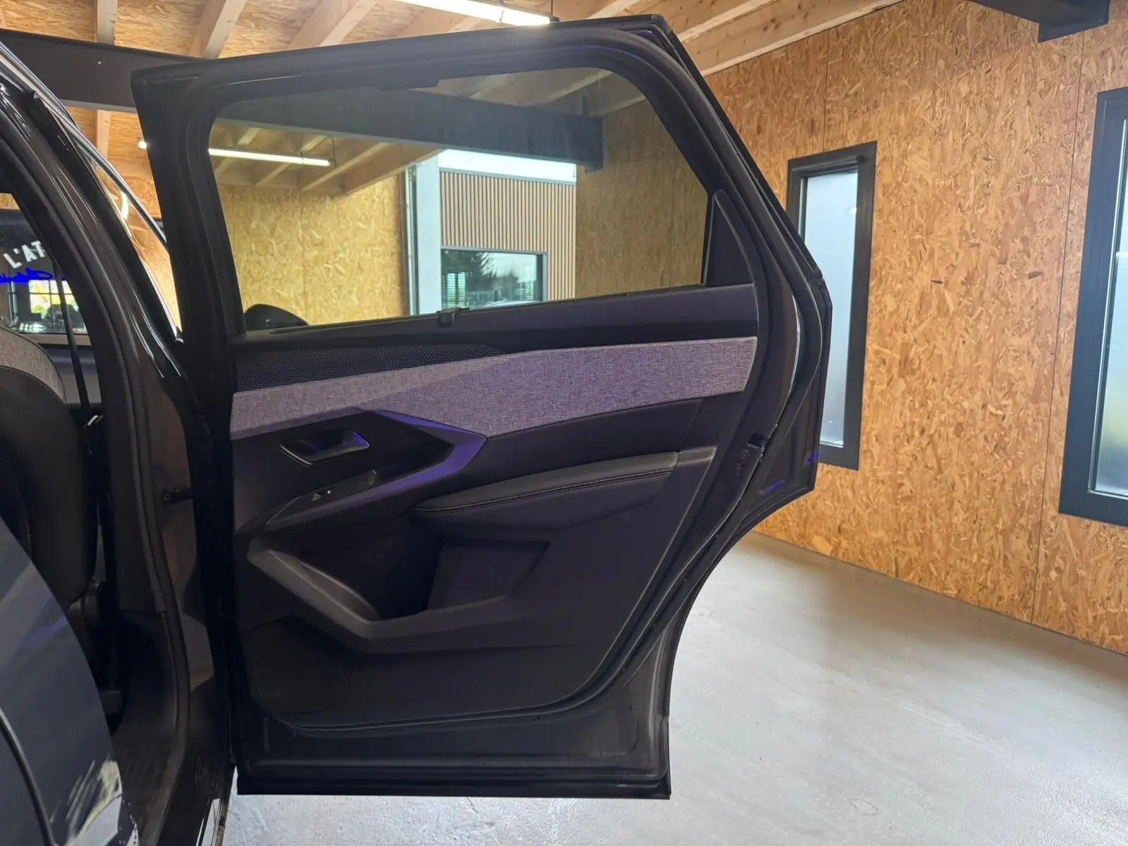 Vue intérieure sur la porte arrière gauche ouverte d’un Peugeot 5008 gris 1.2 Hybrid 136 GT avec habillage tissu gris et noir.