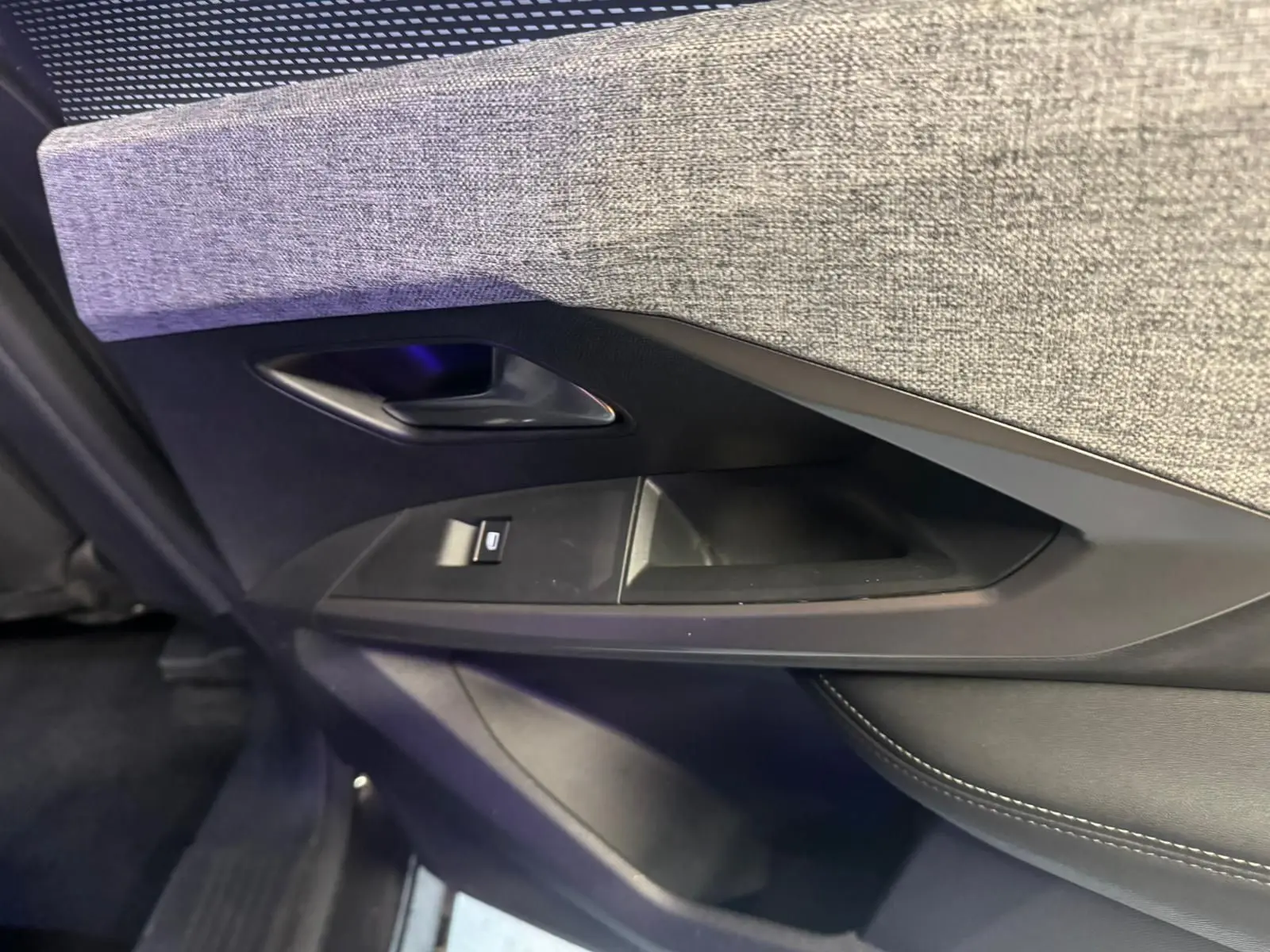 Gros plan sur la garniture intérieure de la porte côté gauche du Peugeot 5008 gris, avec tissu gris et commande de fenêtre.