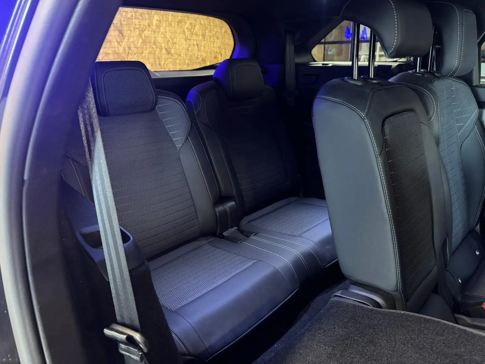 Vue intérieure arrière du Peugeot 5008 gris 2025, montrant les sièges en tissu noir avec surpiqûres blanches.