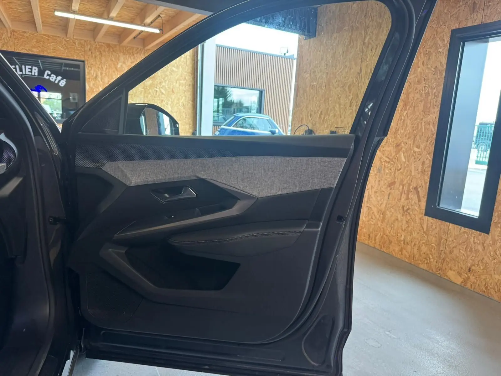 Vue intérieure de la porte avant gauche du Peugeot 5008 gris 2025, avec garniture tissu et plastique noir.
