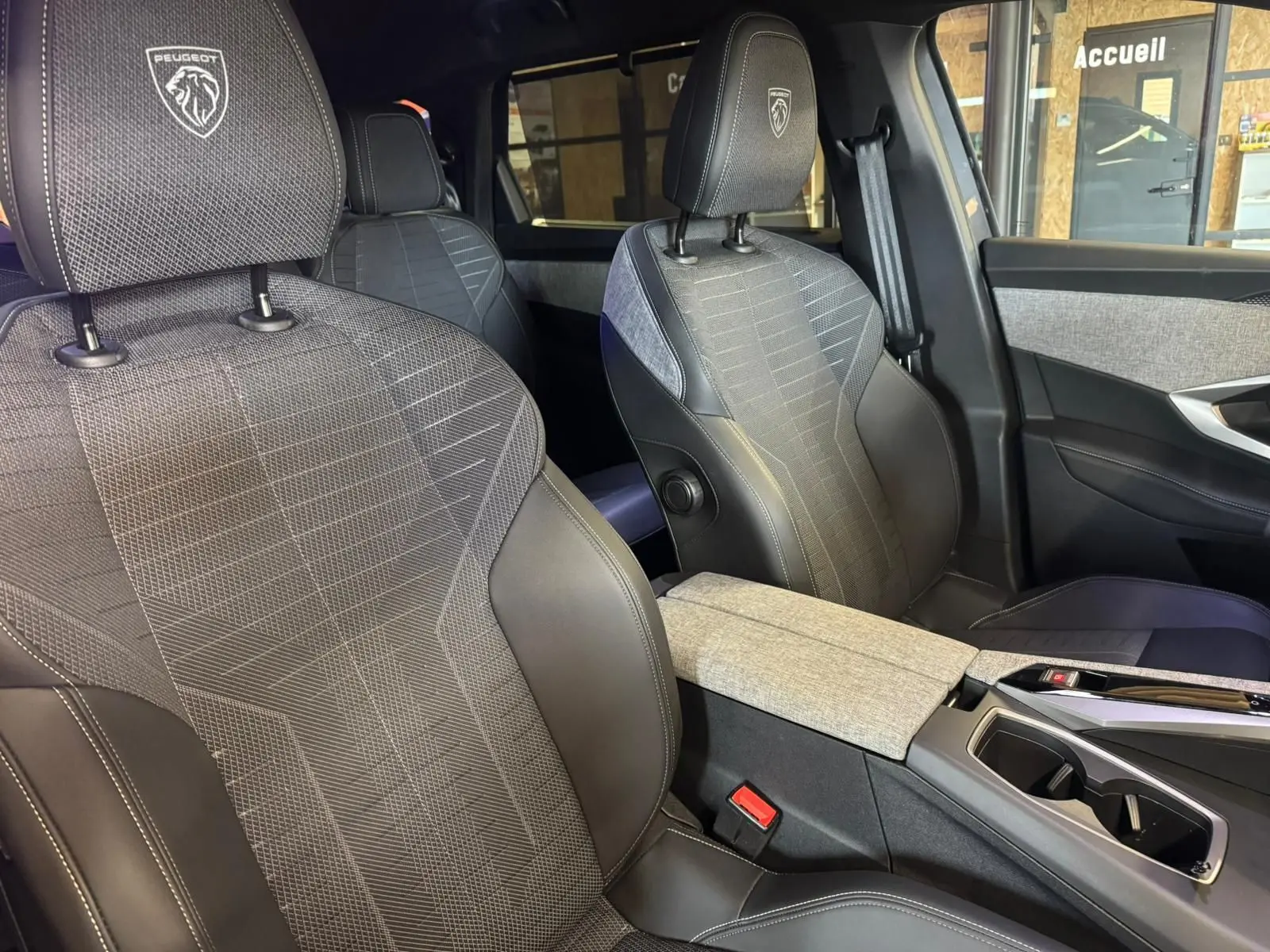 Vue intérieure rapprochée des sièges avant gris tissu et cuir du Peugeot 5008 1.2 HYBRID 136 GT avec logo sur appuie-tête.