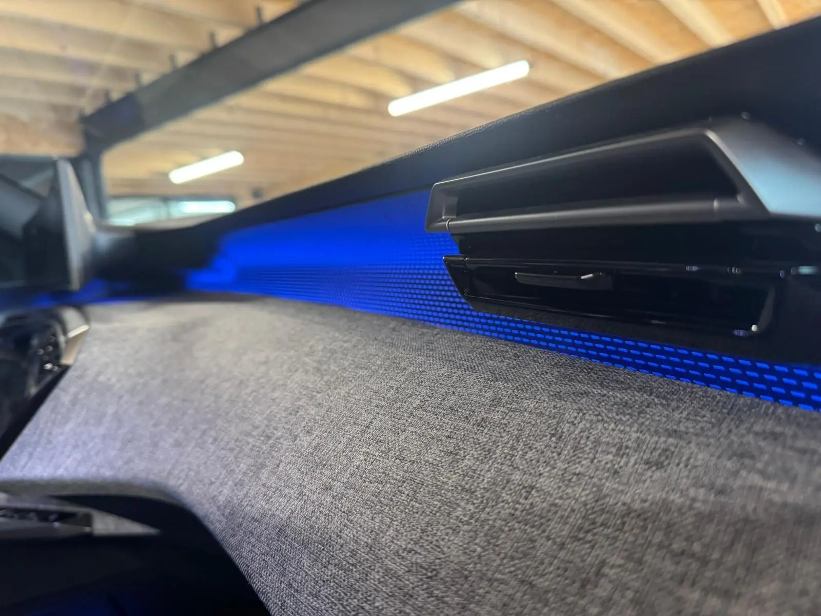 Détail intérieur du tableau de bord du Peugeot 5008 gris 1.2 HYBRID 136 GT avec éclairage d’ambiance bleu.