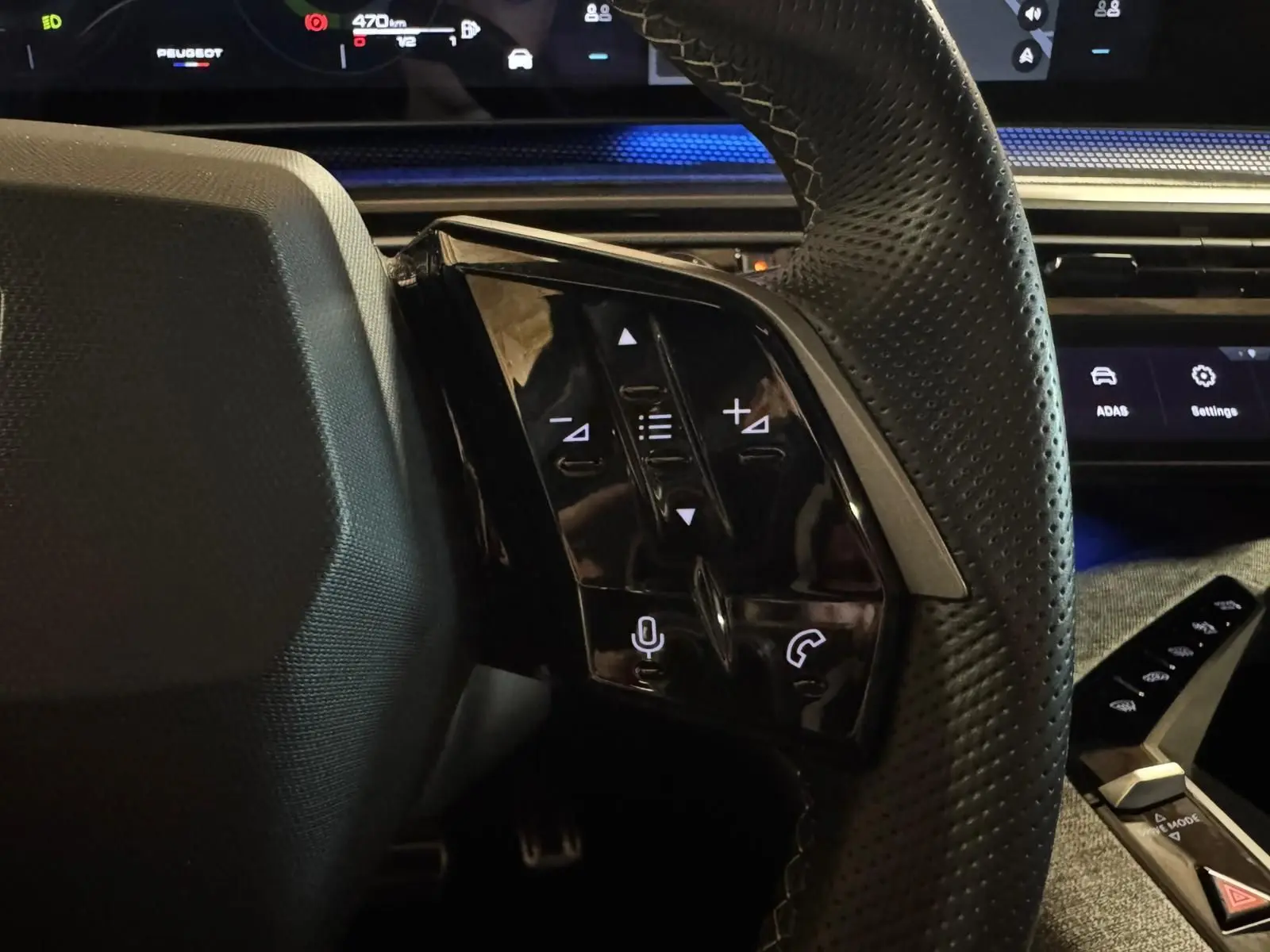 Gros plan sur les commandes au volant à droite du Peugeot 5008 gris 2025, avec tableau de bord digital en arrière-plan.