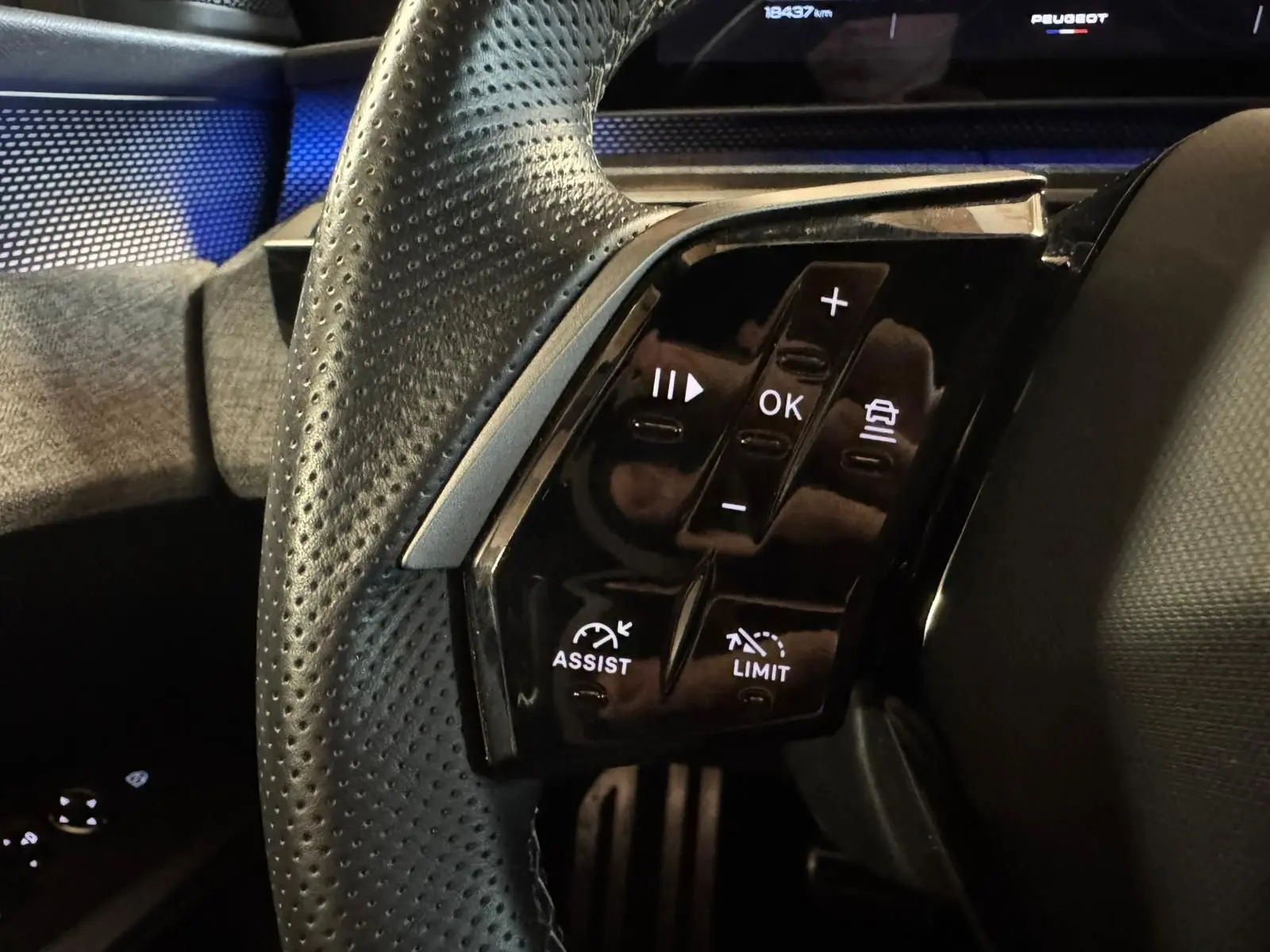 Gros plan sur les commandes au volant côté gauche du Peugeot 5008 gris 1.2 HYBRID 136 GT, affichage digital en arrière-plan.