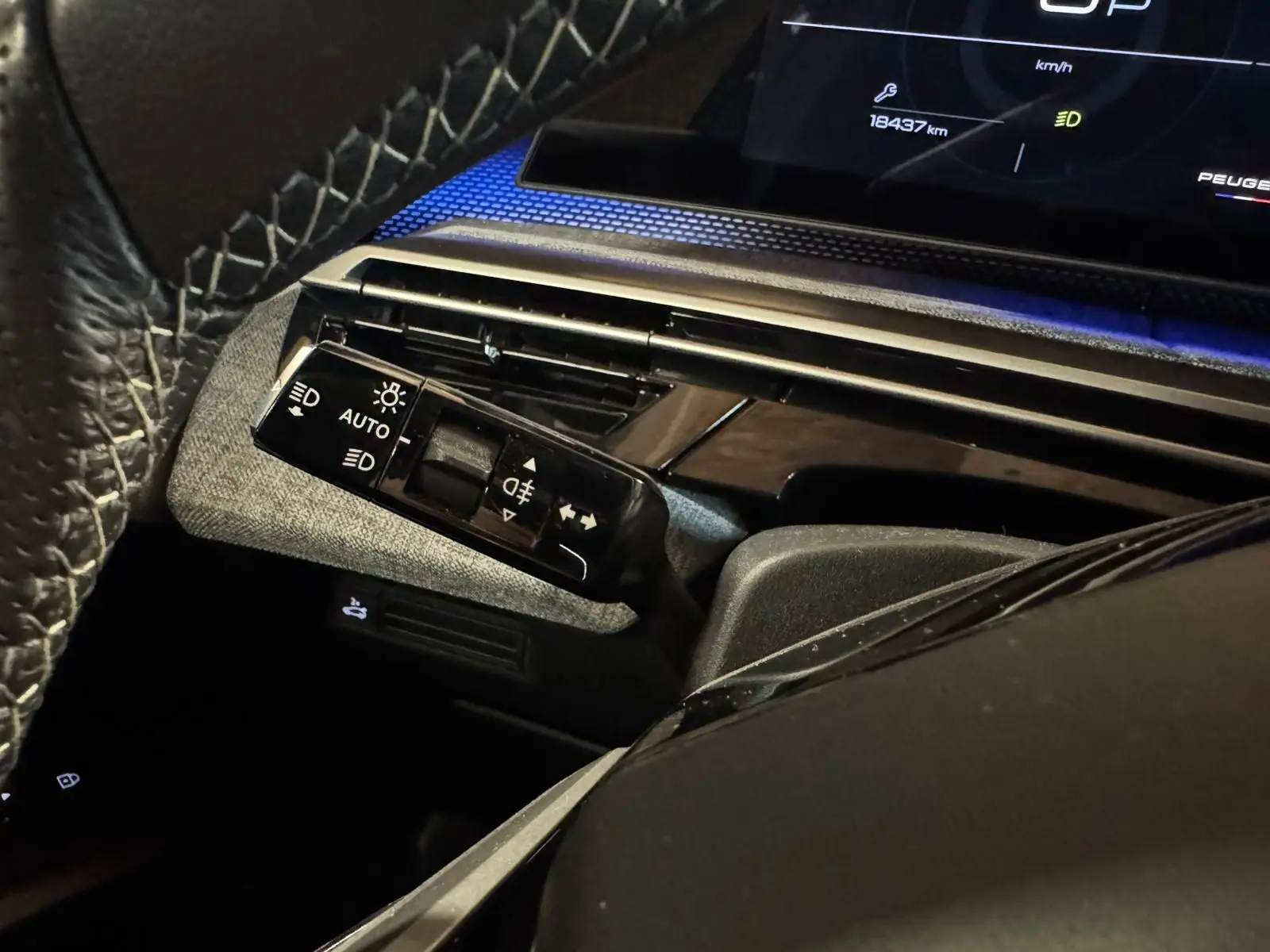 Gros plan sur la commande des feux et clignotants côté gauche du tableau de bord noir du Peugeot 5008 gris 1.2 Hybrid 136 GT.