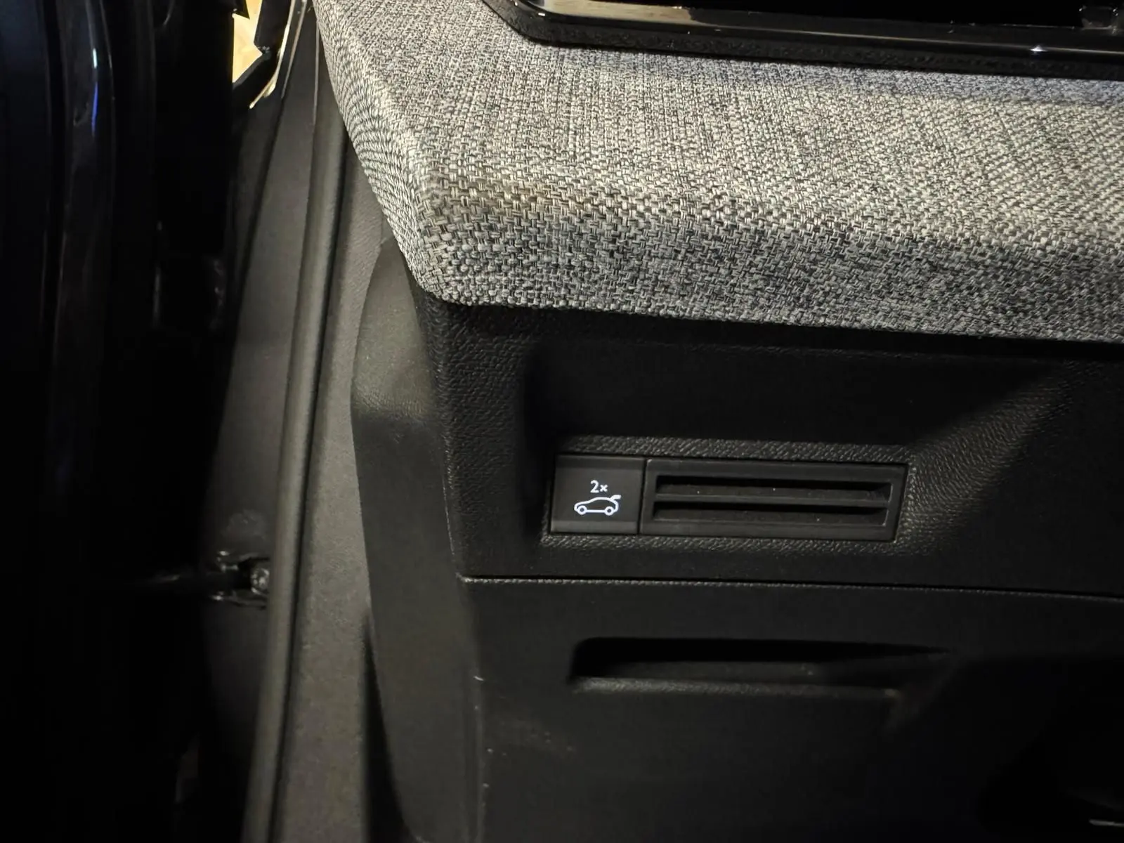 Gros plan sur le bouton d'ouverture du coffre dans l'habitacle du Peugeot 5008 gris, tissu intérieur gris clair.