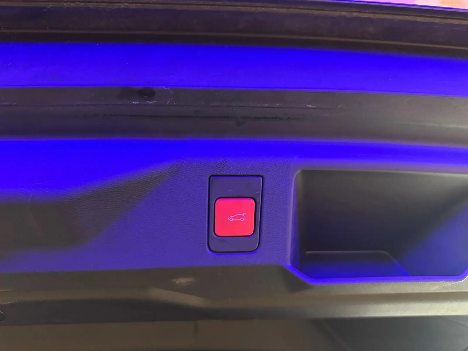 Bouton rouge d'ouverture électrique du coffre sur la plage arrière d'un Peugeot 5008 gris 1.2 Hybrid 136 GT 2025.