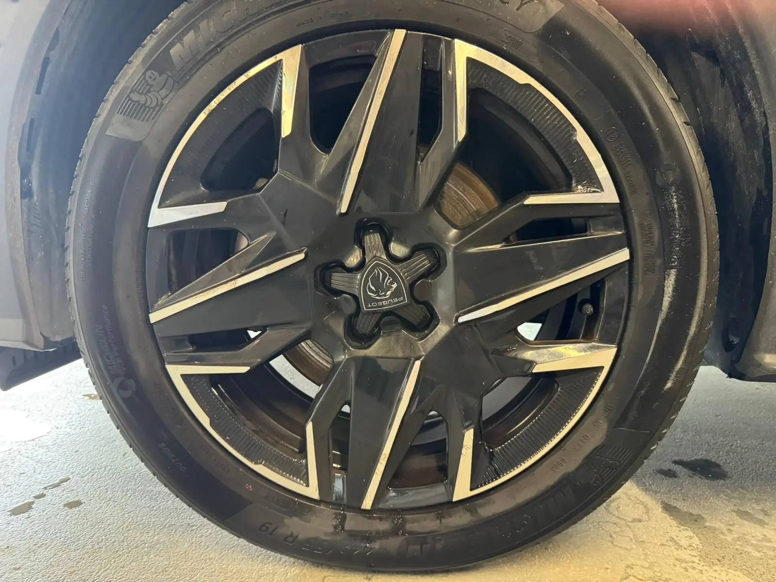 Gros plan sur la jante noire et argentée du Peugeot 5008 1.2 HYBRID 136 GT gris, avec logo Peugeot central visible.