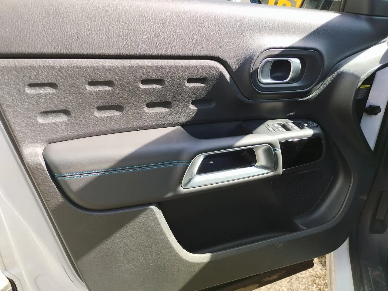 Vue intérieure côté gauche de la porte avant blanche nacrée du Citroën C5 Aircross avec poignée argent et surpiqûres bleues.