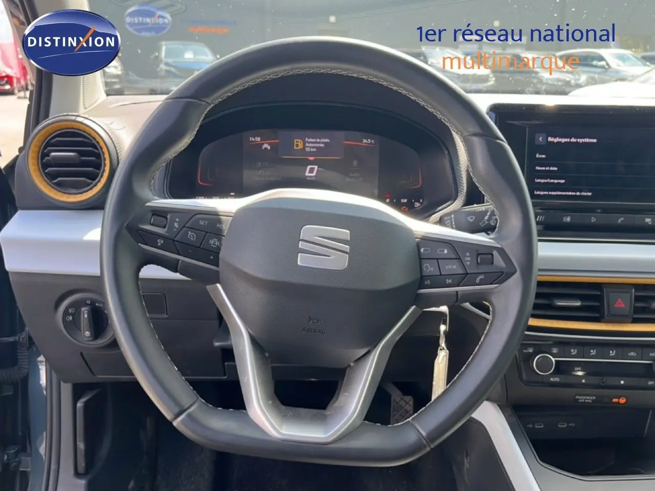 Vue intérieure centrée sur le volant du SEAT Arona 2025, avec tableau de bord numérique et détails orange autour des aérateurs.