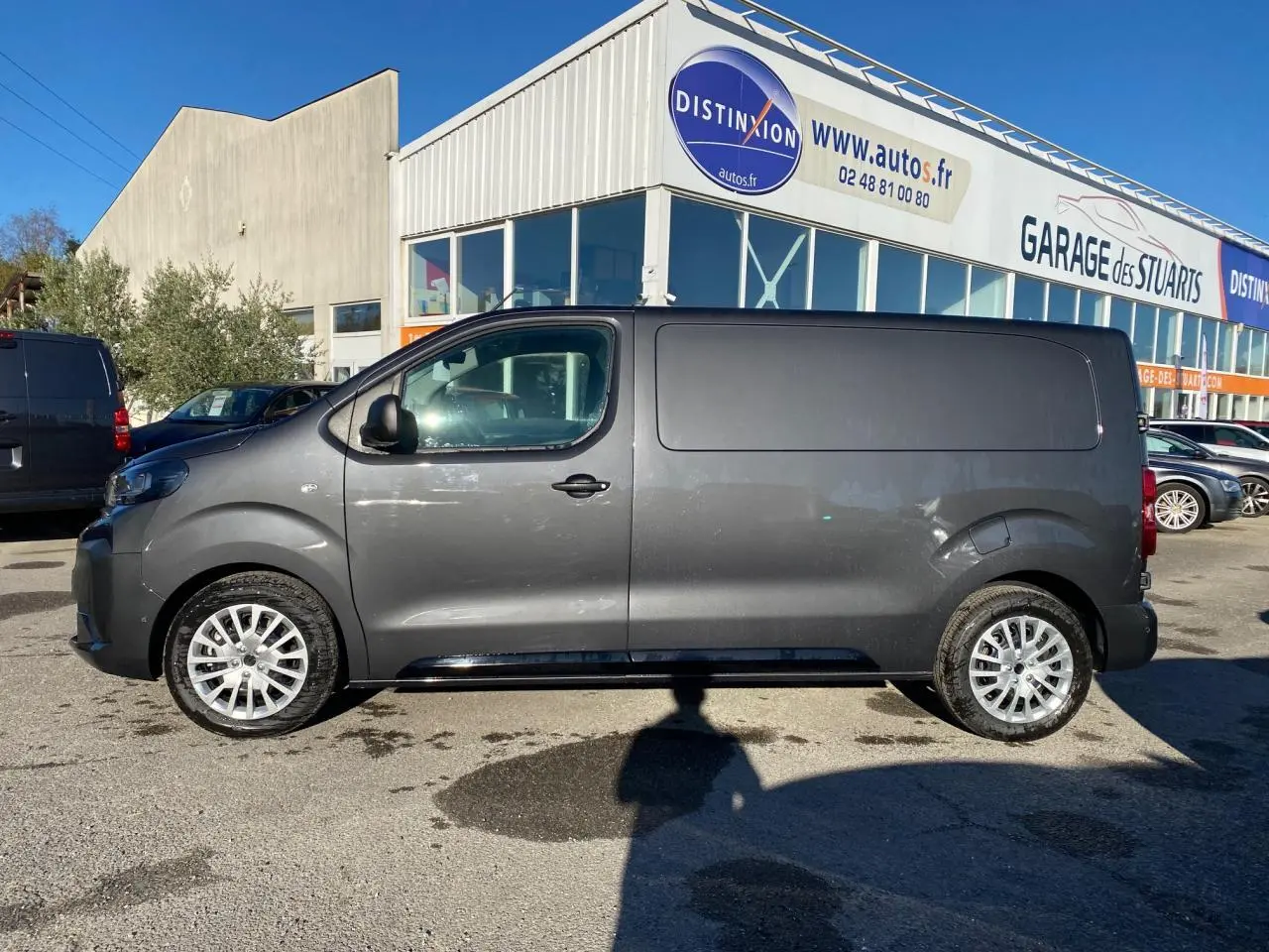 Peugeot Expert Fourgon gris titane vu de profil côté gauche, stationné devant un garage en extérieur.