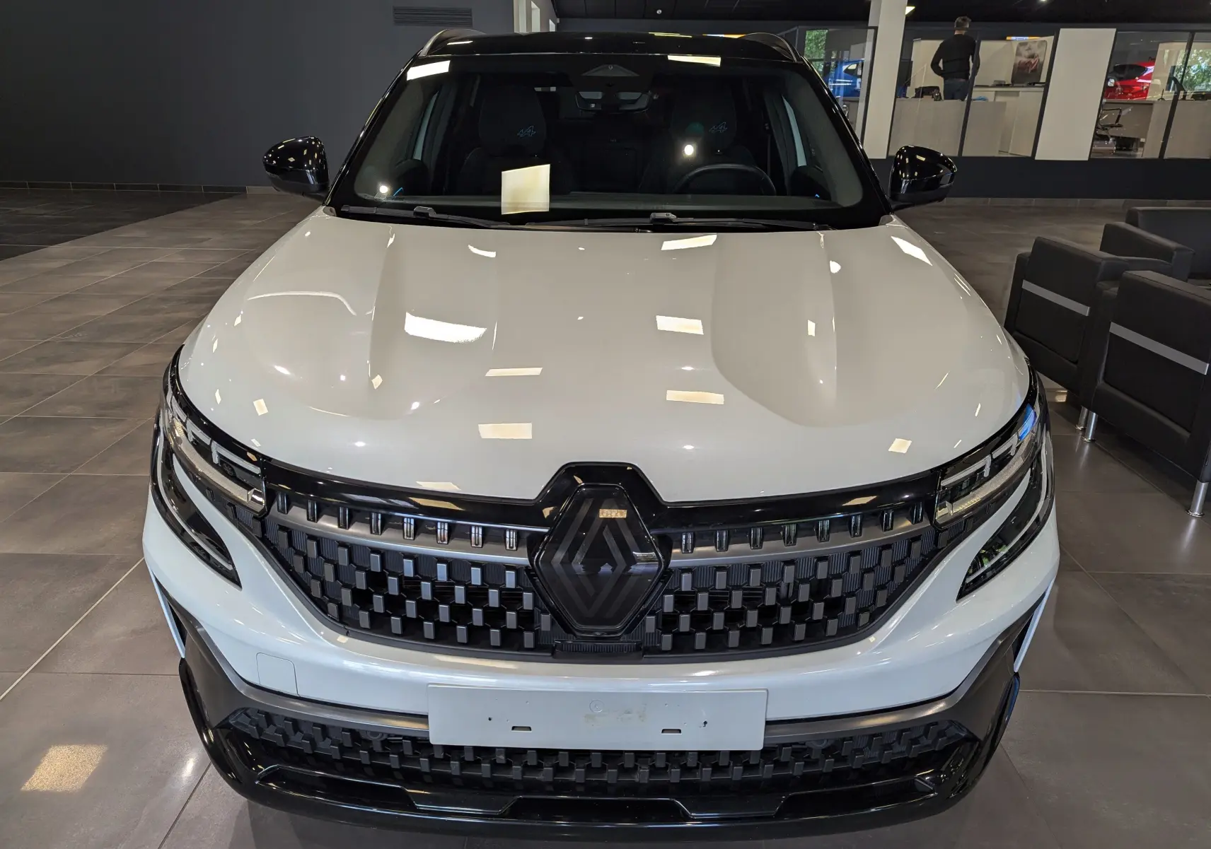 Vue frontale du Renault Austral blanc nacré avec toit noir, mettant en valeur sa calandre noire et ses phares LED fins.