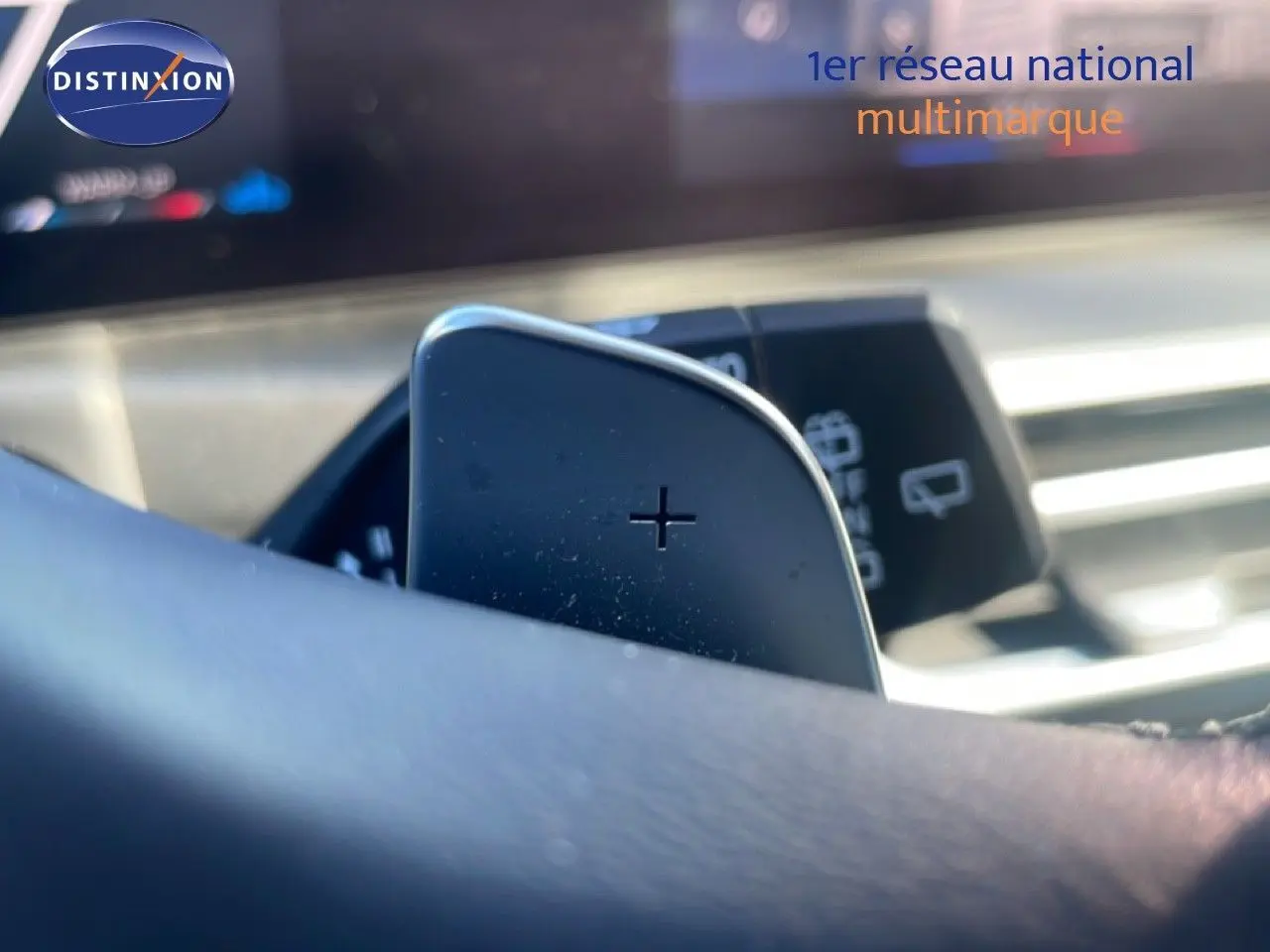 Gros plan sur la palette de changement de vitesse "+" derrière le volant d'une BMW Série 3 Touring noire, intérieur moderne.