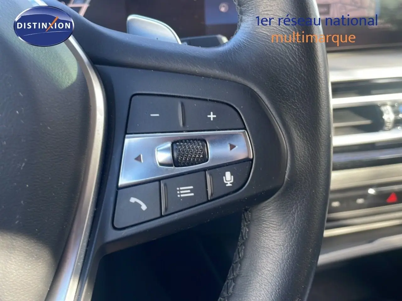 Gros plan sur les commandes du volant en cuir noir de la BMW Série 3 Touring F31 noir saphir, avec tableau de bord en arrière-plan.