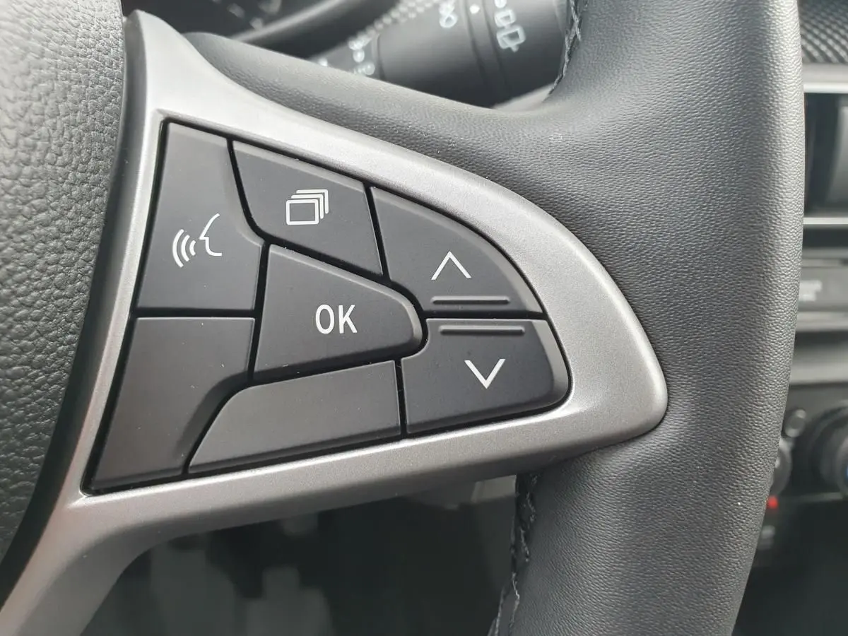 Gros plan sur les commandes multifonctions à gauche du volant en cuir noir de la Dacia Sandero 2025.