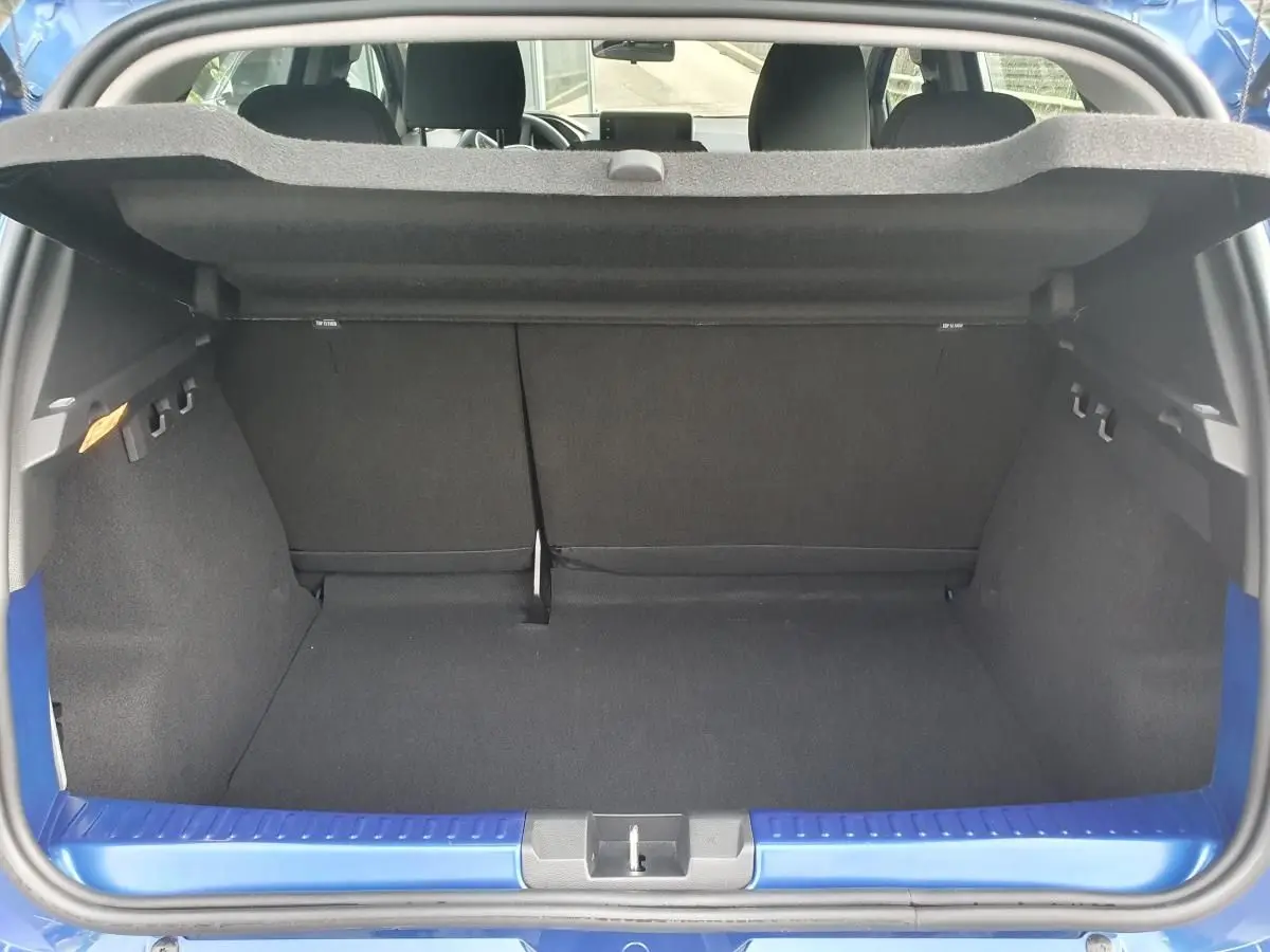 Coffre ouvert vu de l'arrière d'une Dacia Sandero Bleu Iron, montrant l'espace de chargement et la banquette arrière rabattable.