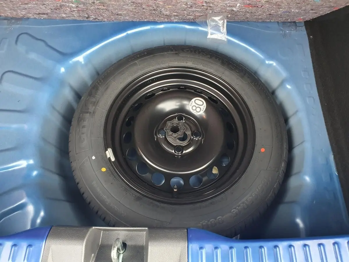 Gros plan sur la roue de secours noire dans le coffre bleu Iron d'une Dacia Sandero 2025.