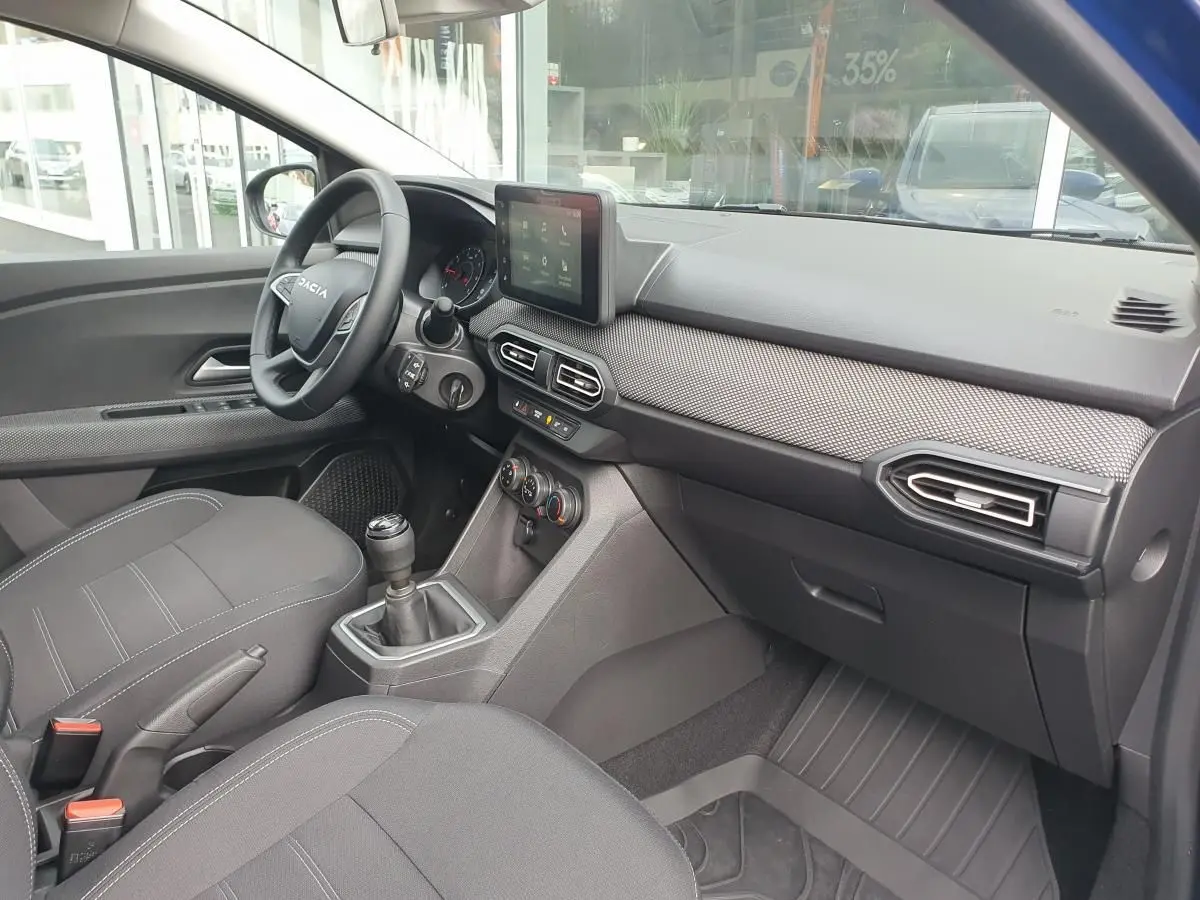 Intérieur de la Dacia Sandero 2025 vu côté passager, avec tableau de bord moderne et siège tissu gris.