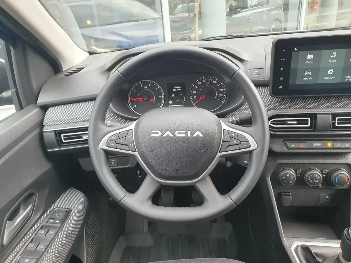 Vue intérieure centrée sur le volant noir de la Dacia Sandero 2025 avec tableau de bord et écran tactile.