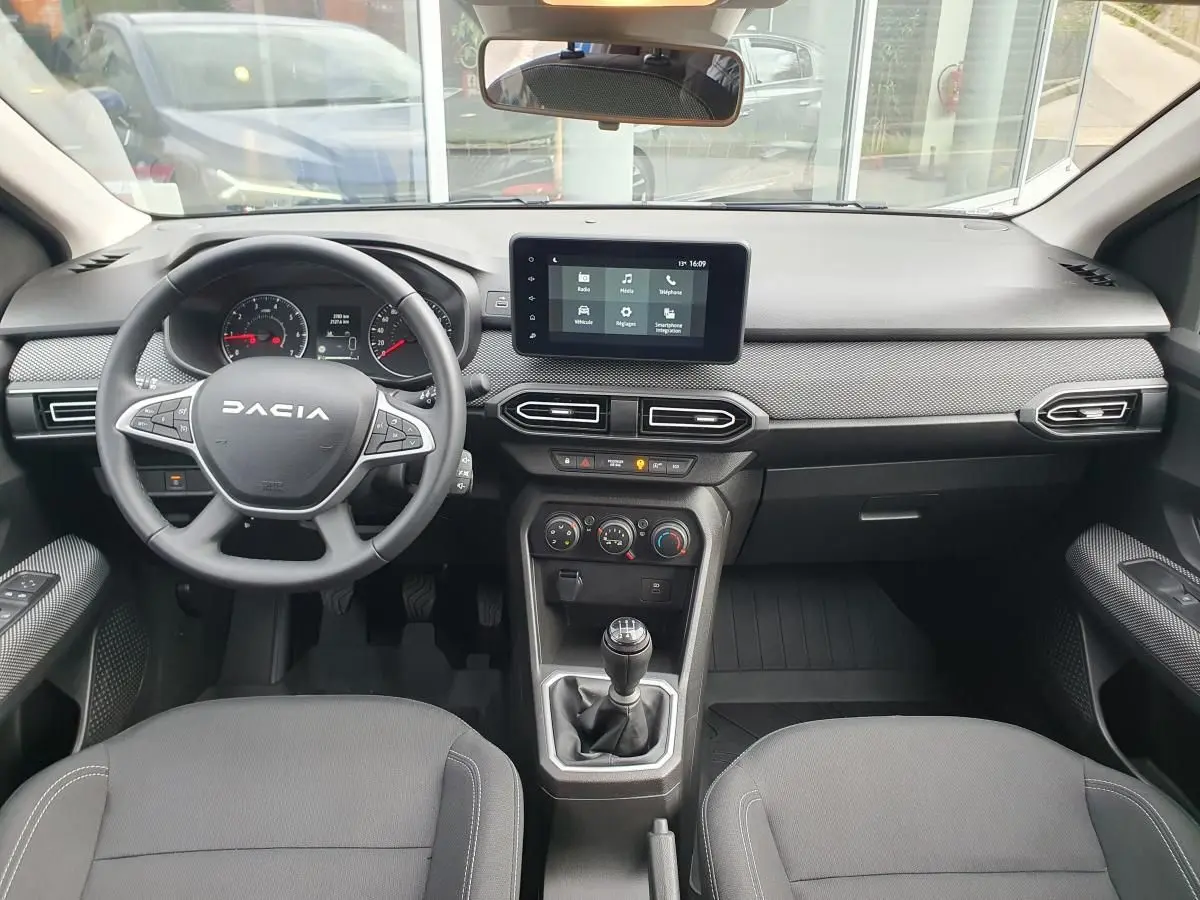 Vue intérieure avant du tableau de bord et volant noir de la Dacia Sandero 2025 avec écran tactile central et boîte manuelle.
