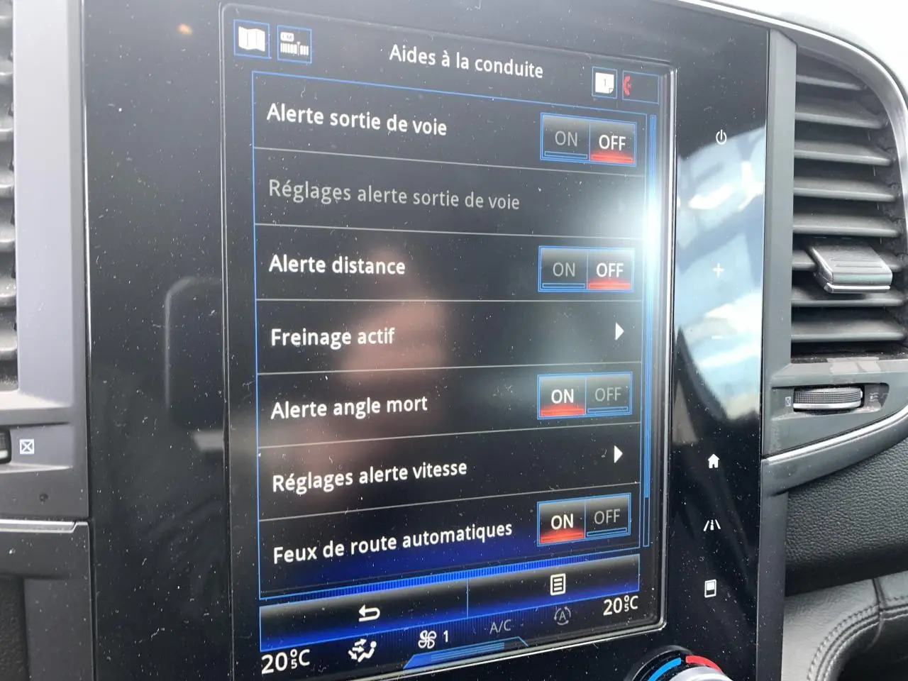 Écran tactile central du Renault Koleos 2019 bleu foncé affichant les aides à la conduite, avec aérateurs latéraux visibles.