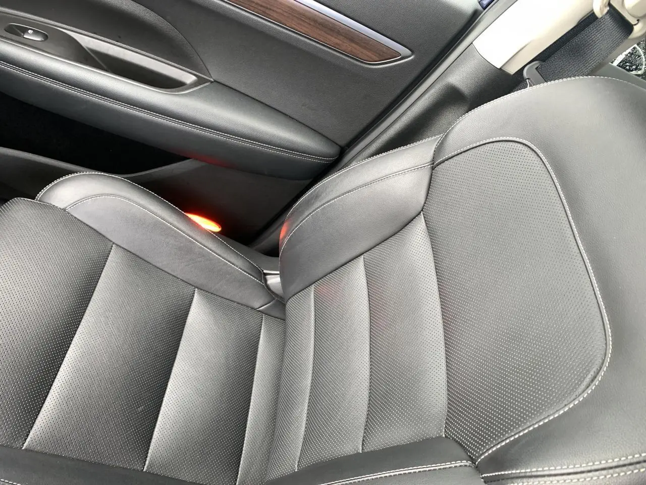 Gros plan sur le siège avant droit en cuir noir avec surpiqûres blanches et insert décoratif bois sur la porte du Renault Koleos.