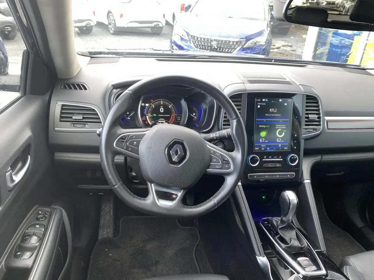 Vue intérieure avant du Renault Koleos 2019, tableau de bord noir avec écran tactile central et volant cuir.