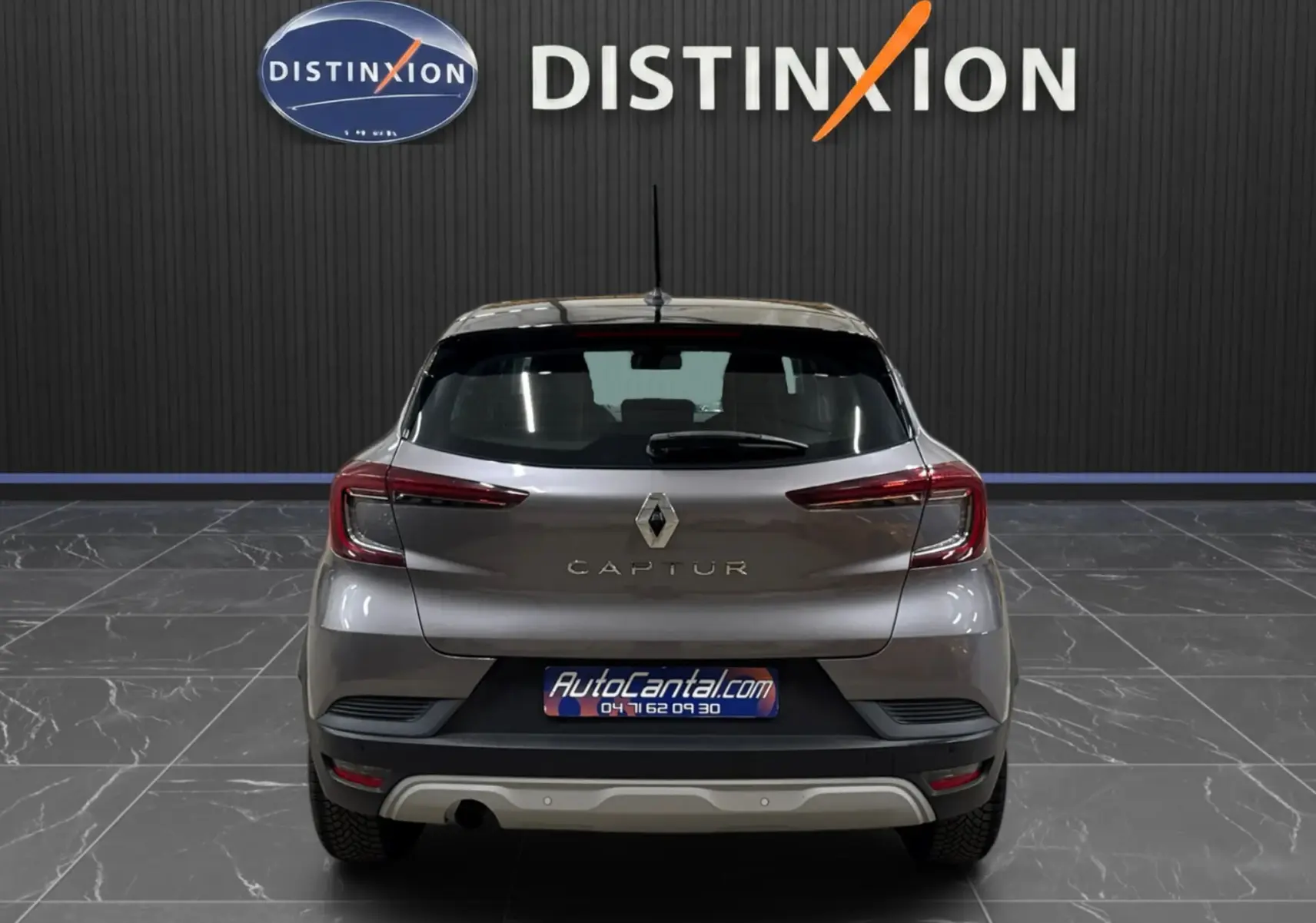 Vue arrière d’un Renault Captur gris foncé avec toit noir, stationné en intérieur devant un mur noir marqué Distinxion.
