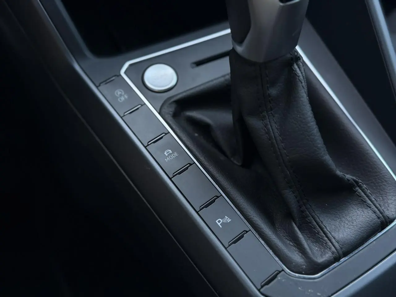Gros plan sur la console centrale noire du Volkswagen Taigo TSI 116 DSG R-Line, avec levier de vitesse cuir et boutons de contrôle.