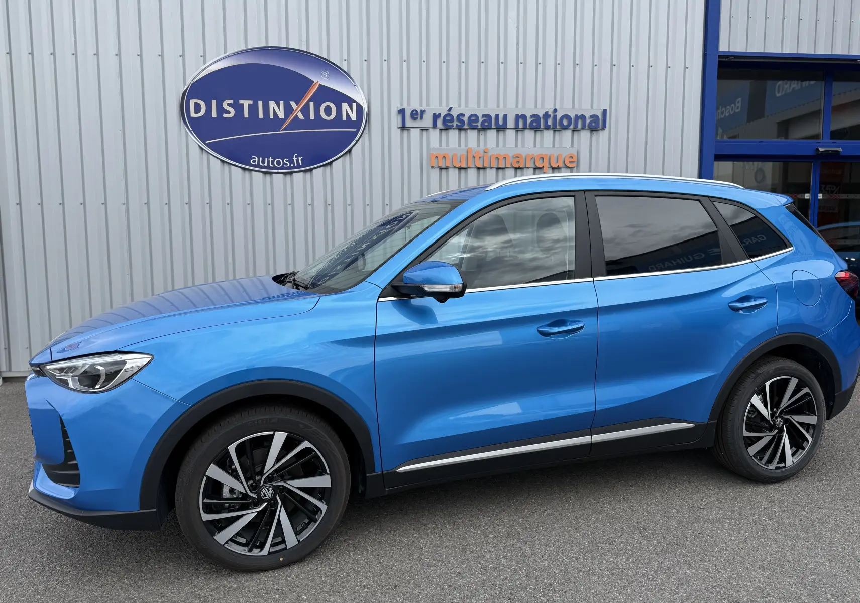 Vue de profil côté gauche du MG ZS 1.5L HYBRID+ 197CH Luxury en bleu Como Metal avec jantes bicolores et vitres teintées.
