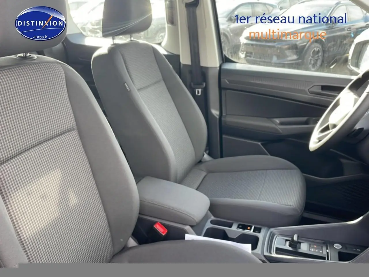 Vue intérieure côté droit du Volkswagen Caddy 2025, sièges tissu gris double grid avec accoudoirs centraux réglables.