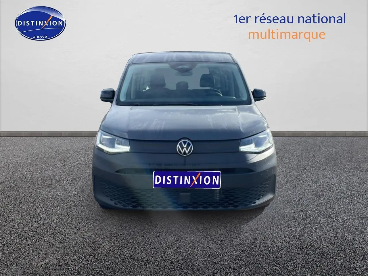 Vue frontale d'un Volkswagen Caddy gris pur 2025 avec phares allumés et calandre épurée.