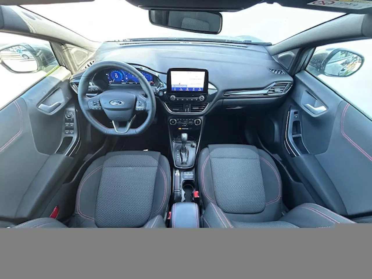 Vue intérieure avant du Ford Puma noir Agate 2023, avec tableau de bord numérique, écran tactile central et sièges noirs à surpiqûres rouges.