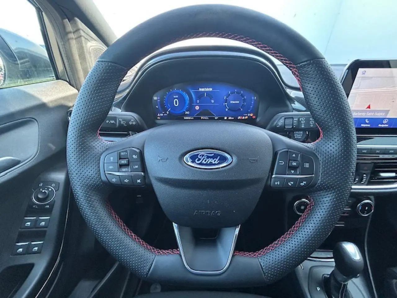 Vue intérieure centrée sur le volant noir perforé avec surpiqûres rouges du Ford Puma 2023, tableau de bord numérique et écran tactile visibles.