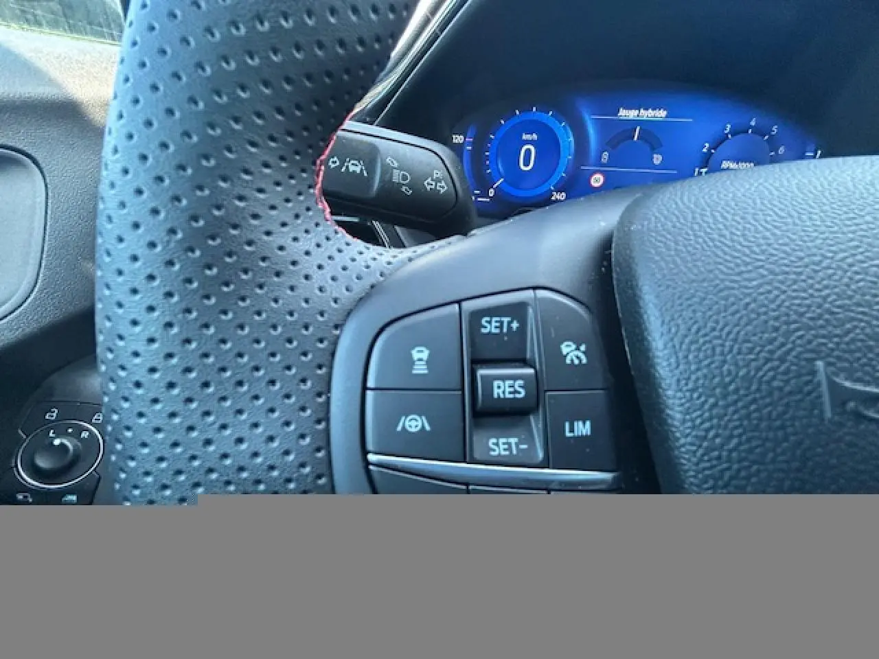 Gros plan sur le volant perforé noir avec surpiqûres rouges et le combiné d'instrumentation numérique bleu du Ford Puma 2023.