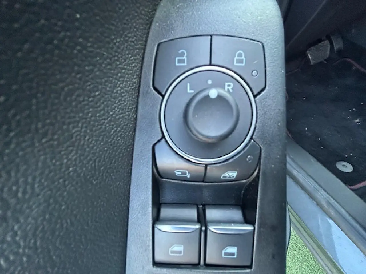 Gros plan sur les commandes de réglage des rétroviseurs et des vitres côté conducteur du Ford Puma noir Agate 2023.