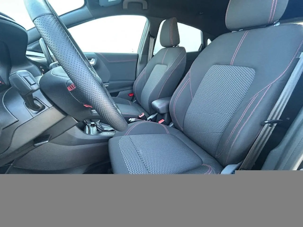 Vue intérieure côté conducteur du Ford Puma noir Agate, sièges tissu avec surpiqûres rouges et volant perforé ST-Line.