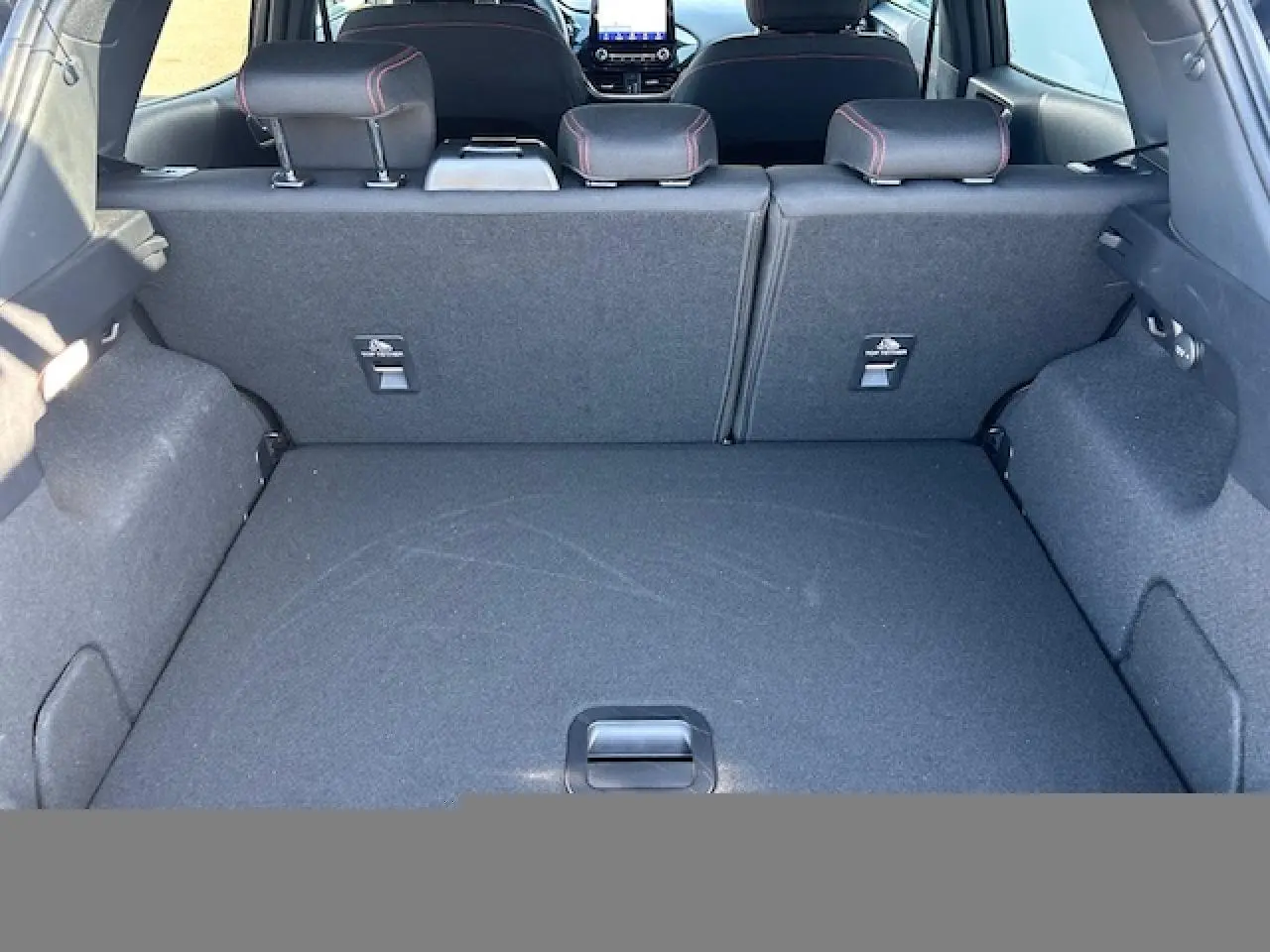 Vue intérieure du coffre du Ford Puma noir Agate, montrant la banquette arrière rabattable avec surpiqûres rouges visibles sur les appuie-têtes.