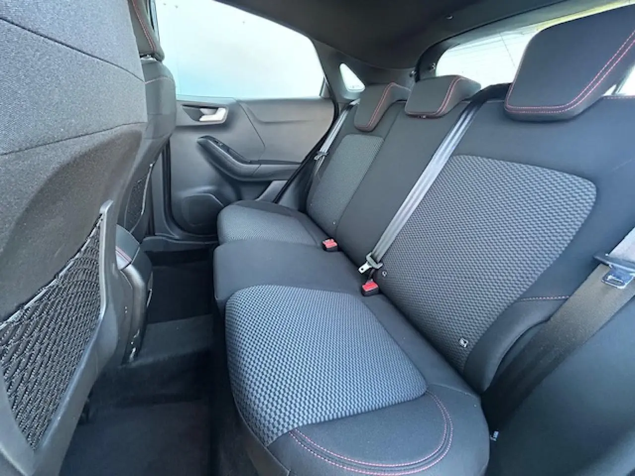 Vue intérieure arrière côté droit du Ford Puma noir agate, banquette tissu noir avec surpiqûres rouges et appuie-têtes intégrés.