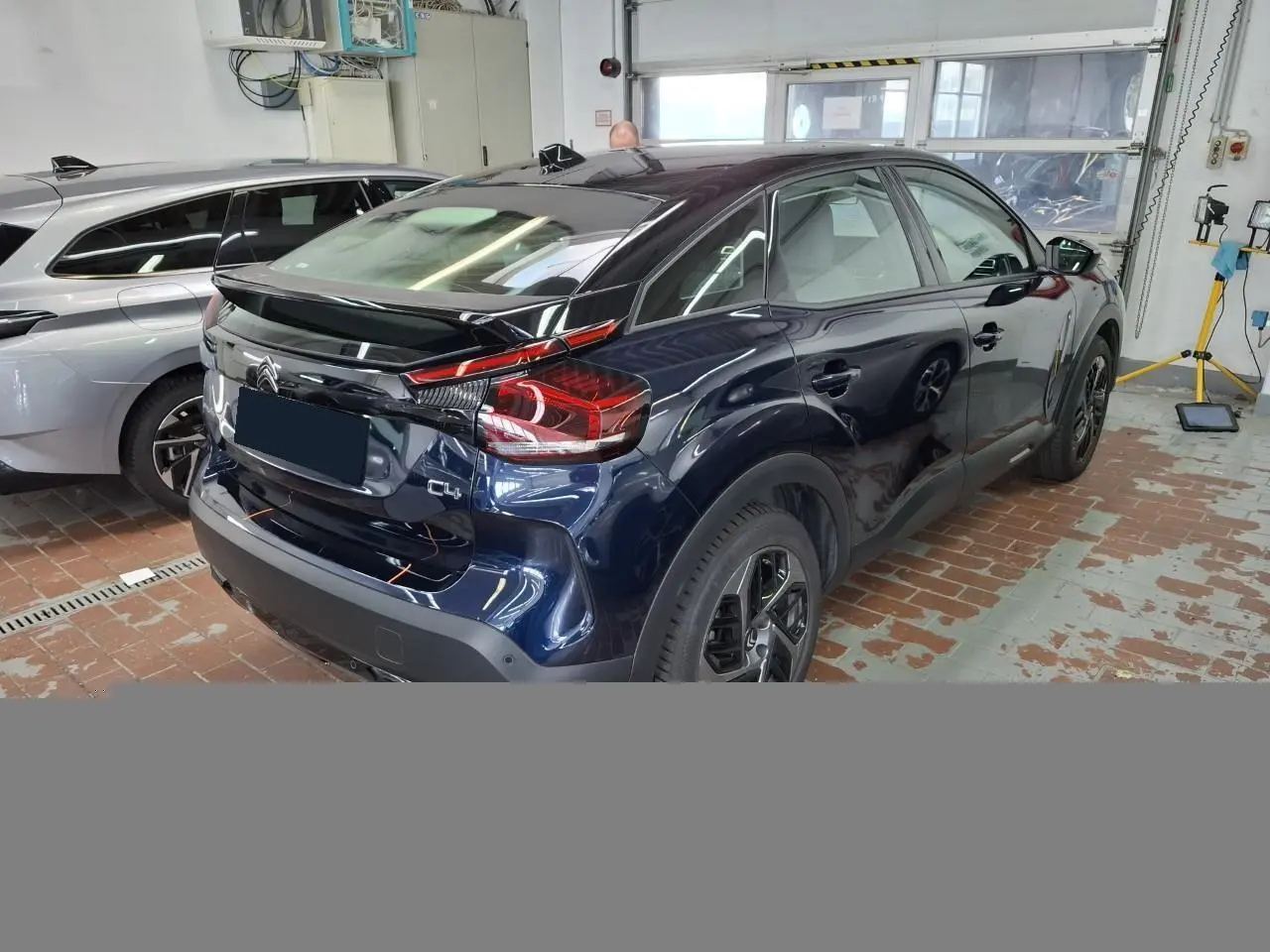 Vue 3/4 arrière droite d'une Citroën C4 2024 bleu Eclipse avec toit noir Perla dans un garage.