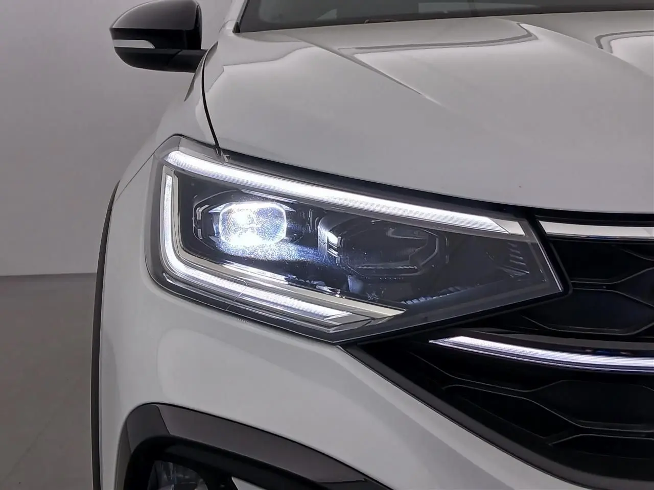Gros plan sur le phare avant gauche allumé d'un Volkswagen Taigo blanc pur avec toit noir et calandre noire.