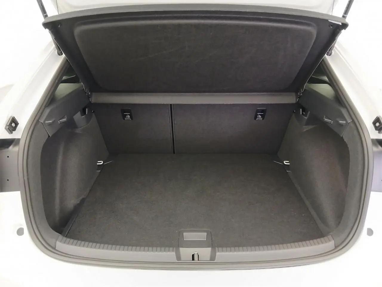 Coffre ouvert vu de face d'un Volkswagen Taigo blanc pur, intérieur noir avec cache-bagages relevé.