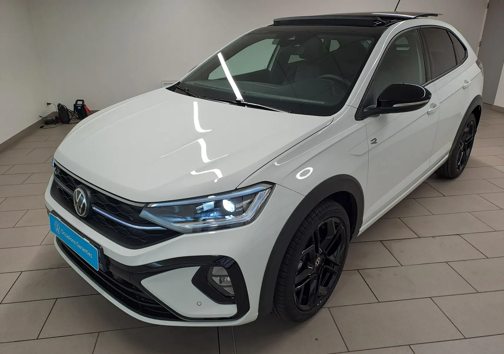Volkswagen Taigo blanc pur avec toit noir en 3/4 avant droit, jantes noires et phares LED allumés.